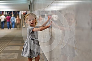 A little girl walks along the underground passage of the subway. A child near a gray wall. Children& x27;s safety in a public