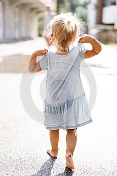 Little girl walks barefoot through the puddles. Back view