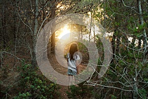 Little girl walks through a pine forest towards the light at sunset