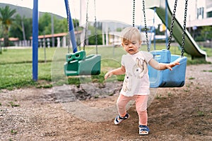 Little girl walks on the playground against the background of a swing