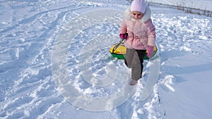 A little girl walks through the snow, pulling with her tubing