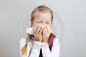 Little girl in a warm scarf blows her nose. Sick child on a gray background. Cold season