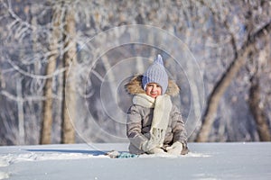 Little girl in warm wear sits in snow in winter