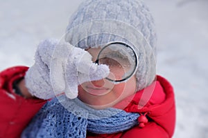 Little girl in warm winter clothes with a magnifying glass in her hand investigate  details of nature . Winter outdoor kids