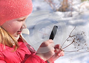 Little girl in warm winter clothes with a magnifying glass in her hand investigate  details of nature . Winter outdoor kids