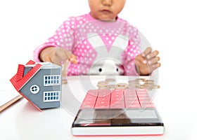 The little girl was fiddling with the coins on the table, the model of the small house and a calculator