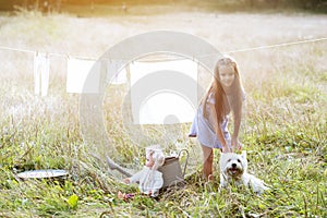 Little girl wash retro doll clothes and playing with her funny puppy, summer nature outdoor. Washing, children`s games