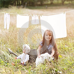 Little girl wash retro doll clothes and playing with her funny puppy, summer nature outdoor. Washing, children`s games