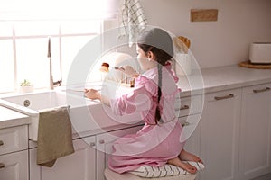 Little girl washing dishes in kitchen at home