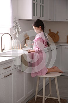 Little girl washing dishes in kitchen at home