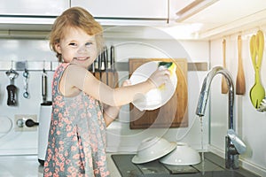 Little girl washing dishes with sponge in kitchen sink at home