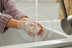 Little girl washing hands with liquid soap at home, closeup
