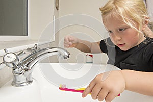 Little Girl Washing Toothbrush Under Running Water in Bathroom S