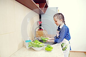 Little girl is washing vegetables for salad closeup