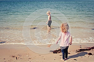 A little girl watches her brother exploring and playing in the sea