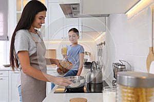 Little girl watching mother cooking in kitchen. Single parenting