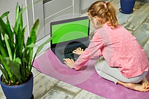 Little girl watching online video on laptop and doing stretching, fitness exercises at home