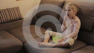 Little girl watching TV and eating chips sitting on sofa