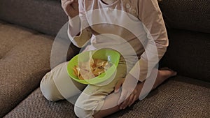 Little girl watching TV and eating chips sitting on sofa