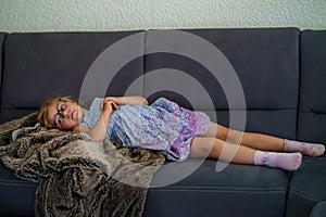 Little girl watching TV lying on couch. Preschool child with glasses enjoying cartoons or film