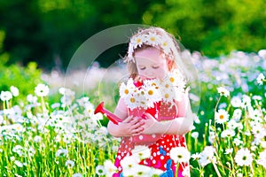 Little girl with water can in a daisy flower field.