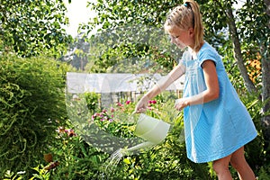 Little girl watering the flowers in the family garden at a summer day, very rural scene