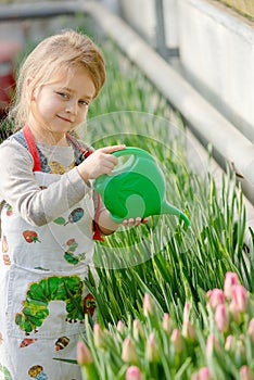 Little girl watering flowers in a greenhouse.