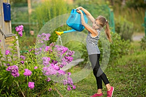 Little girl watering the flowers near the country house. Summer.