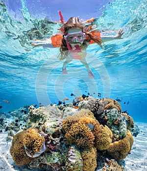 A little girl with waterwings snorkels over a colorful reef in the Indian Ocean