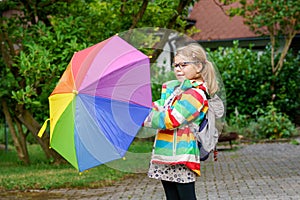 Little girl on way to elementary school or kindergarden. Preschool Child with colorful rainbow umbrella and waterproof