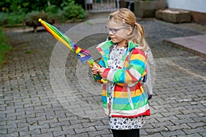 Little girl on way to elementary school or kindergarden. Preschool Child with colorful rainbow umbrella and waterproof