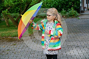 Little girl on way to elementary school or kindergarden. Preschool Child with colorful rainbow umbrella and waterproof