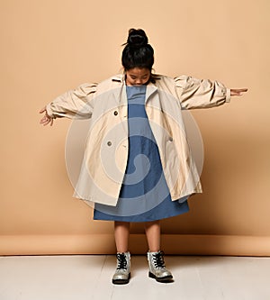 Little girl wearing autumn trench coat holding handbag, over gray background