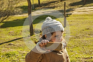 Little girl wearing grey bonnet taking a selfie with mobile