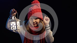 Little girl wearing knitted winter hat and scarf lighting with lantern