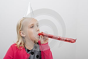 Little girl wearing party hat blowing noisemaker at home photo