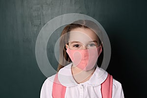 Little girl wearing protective mask and backpack near chalkboard. Child safety