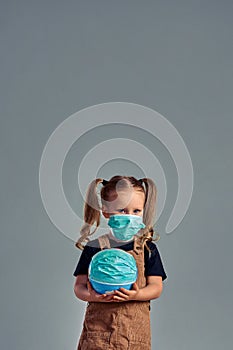 Little girl wearing protective mask holds planet Earth. The concept of a global warming or coronavirus pandemic