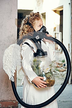 Little girl wearing a respirator mask breathes clean air. the child holds a flower in a vacuum jar. ecology concept