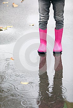 Little girl wearing rubber boots standing in puddle on rainy day, focus of legs.