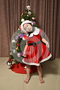 A little girl wearing a Santa Claus costume play in front of a Christmas tree tree