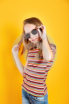 Little girl wearing sunglasses smiling and posing on yellow background