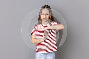 Little girl wearing T-shirt showing time out gesture, looking at camera deadline with test in school