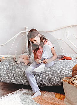 Little girl wears socks sitting on a bed in her bedroom. The kid`s going to school. Independent children