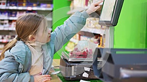 a little girl weighs candy on scales in the store.