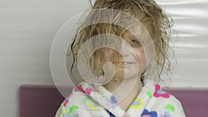 Little girl with wet hair in bathrobe making faces. Smiles after bathing