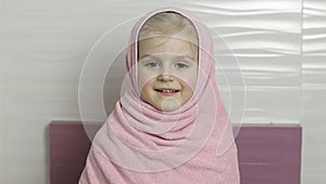 Little girl with wet hair is hiding in pink towel. Smiles after bathing