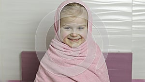 Little girl with wet hair is hiding in pink towel. Smiles after bathing