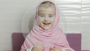 Little girl with wet hair is hiding in pink towel. Smiles after bathing