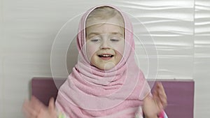 Little girl with wet hair is hiding in pink towel. Smiles after bathing